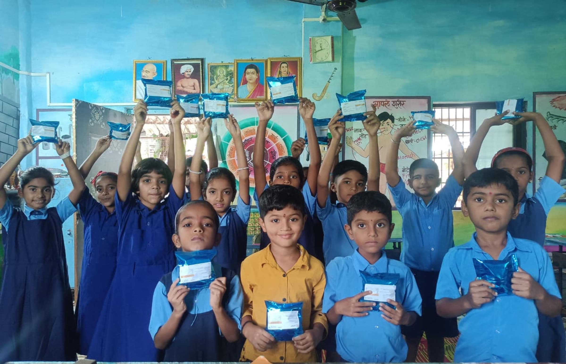 Schoolchildren stand together holding up their nutrition sachets in class.